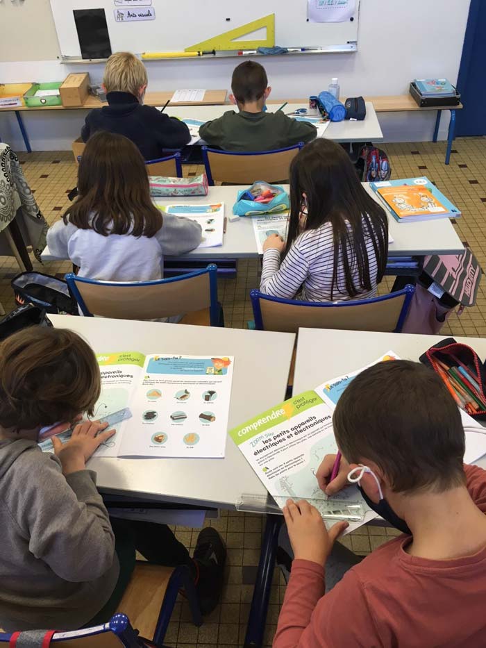 6 élèves de dos tracent une ligne avec leur règle dans leur cahier d'activités